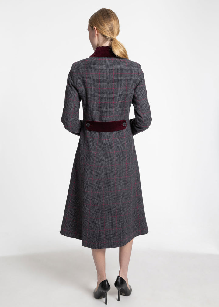 A woman viewed from the back wearing a long gray plaid coat with a dark red velvet collar and waist belt, paired with black heels, against a plain white studio background.