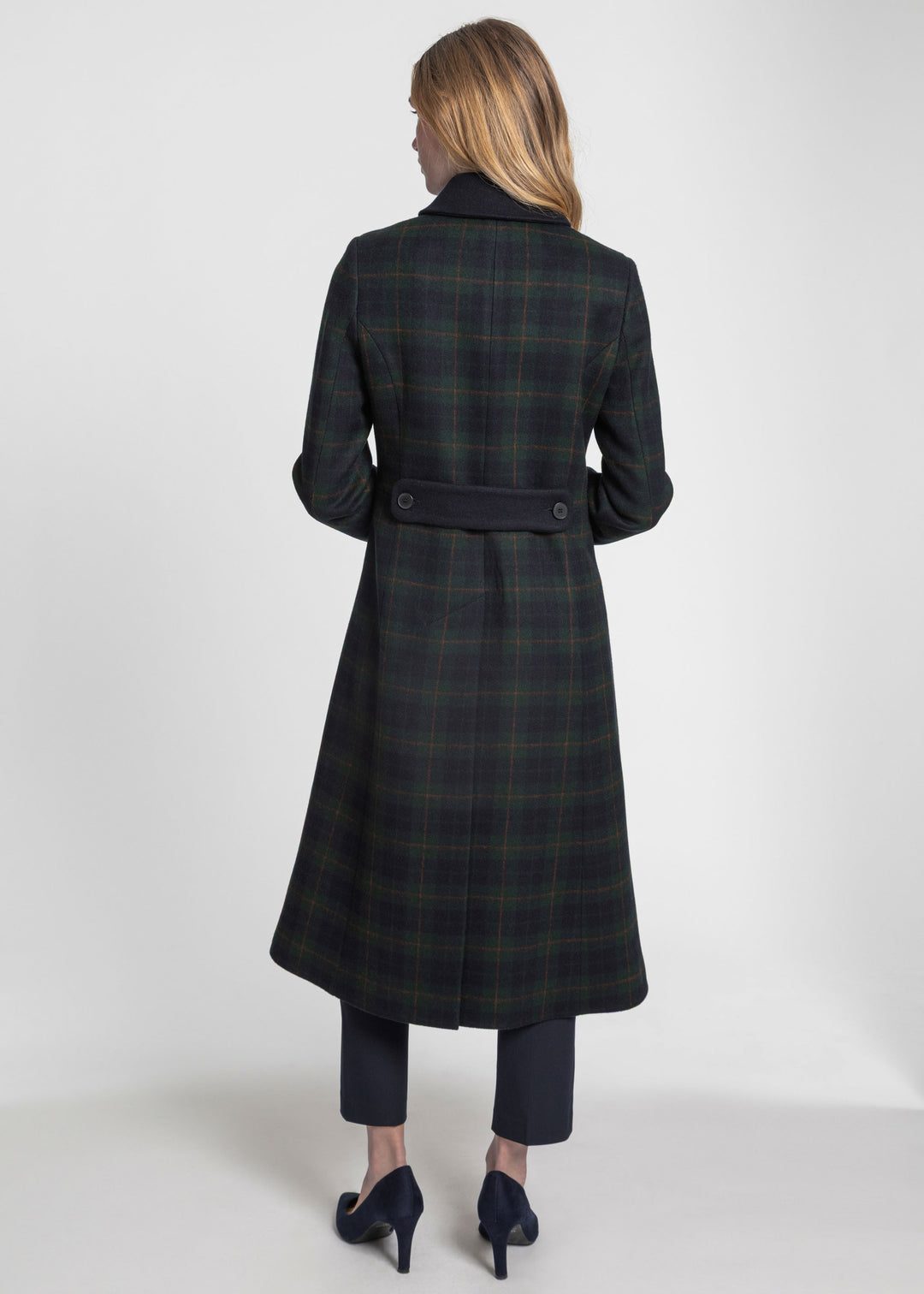 A back view of a woman wearing a navy and green plaid coat with a navy black belt and collar accent.