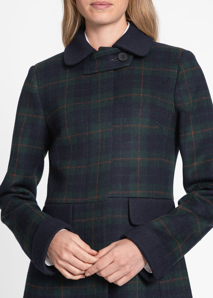 A close-up of a model wearing a dark navy and green plaid wool coat with a single-button collar and flap pockets.