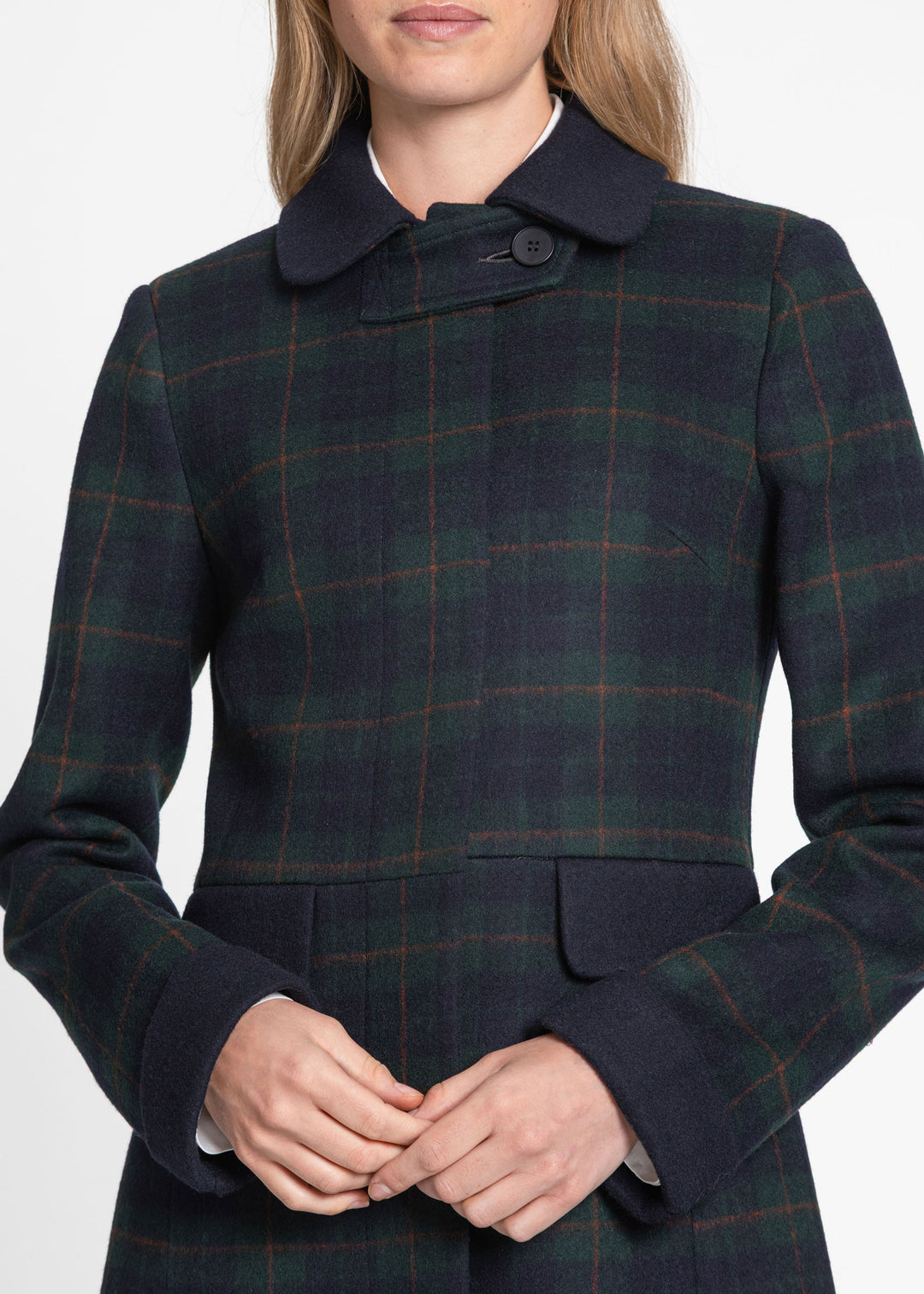 A close-up of a model wearing a dark navy and green plaid wool coat with a single-button collar and flap pockets.