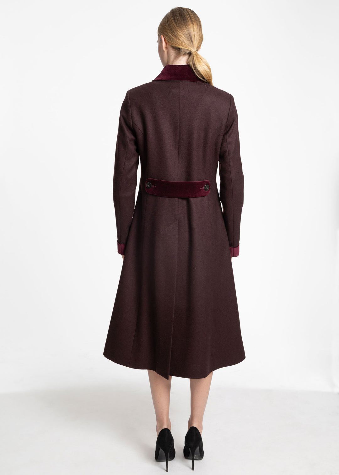 Back view of a woman wearing a mulberry coat with burgundy velvet contrast on the back belt, collar, and cuffs.