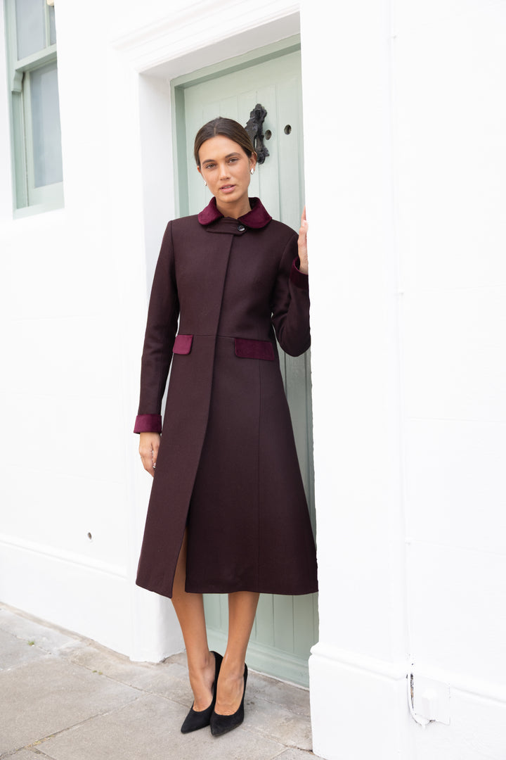 Woman wearing a mulberry red coat with pinkish-red velvet accents on the collar, sleeves, and pockets.