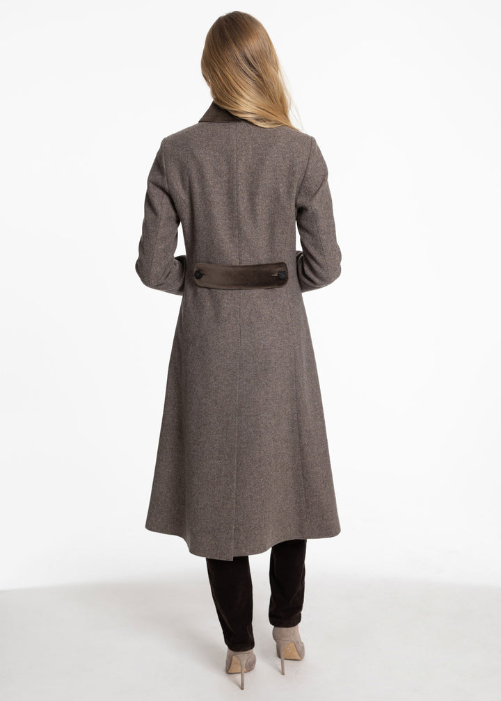 A woman viewed from behind wearing a long taupe-brown wool coat with a dark brown belt, paired with black pants and beige heels, against a plain white studio background.