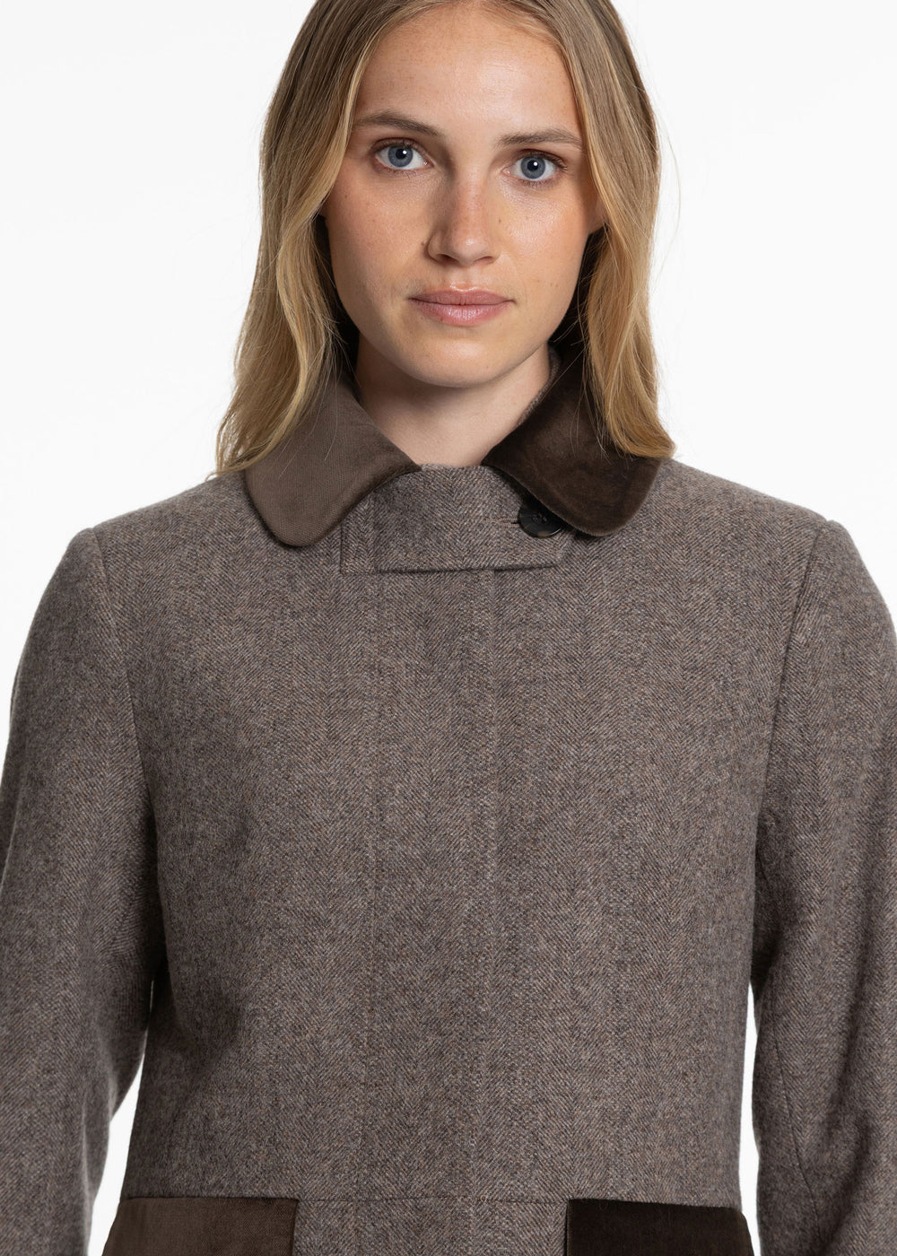 Woman wearing a purple-brown herringbone coat with brown velvet accents. 
