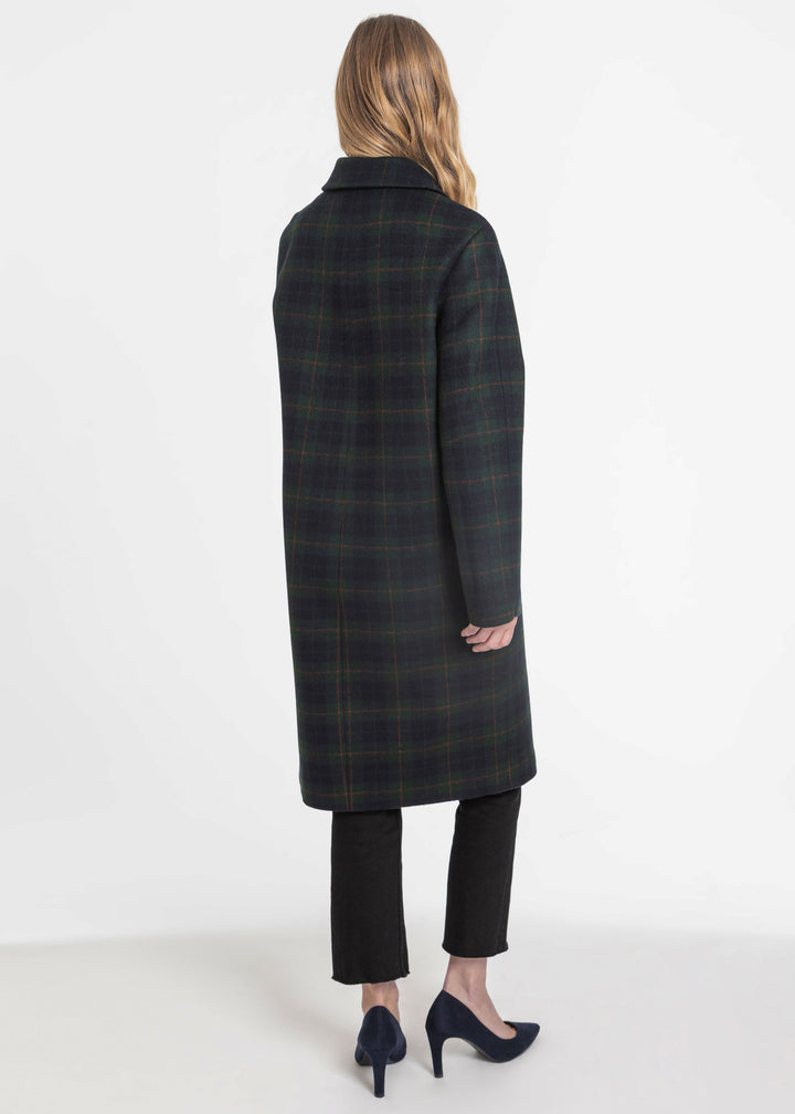 Side view of a woman wearing a navy and green check coat with black pants and black heels.