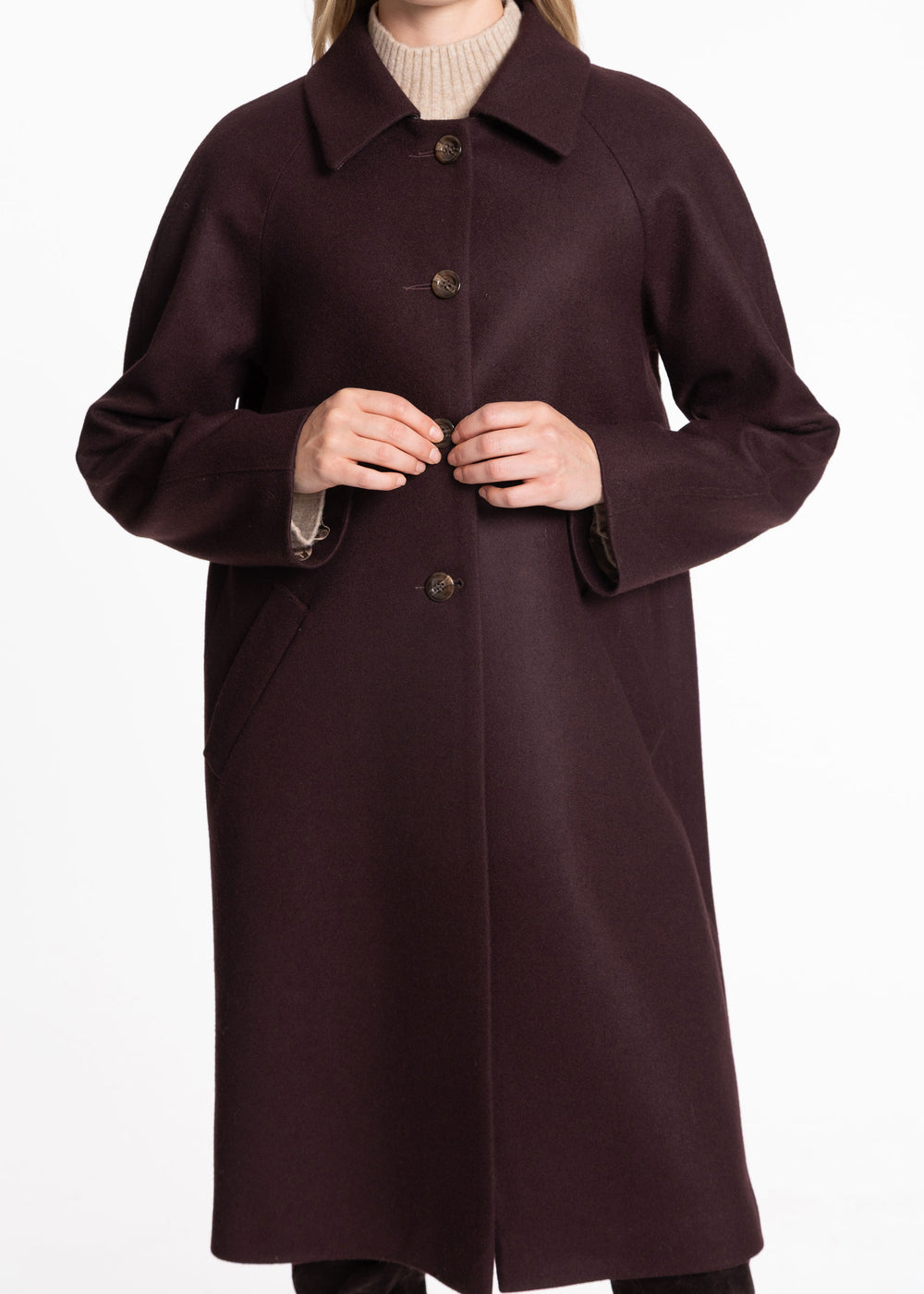 A woman wearing a long, mulberry colored wool coat over a cream turtleneck sweater, shown from the neck down against a plain white background.