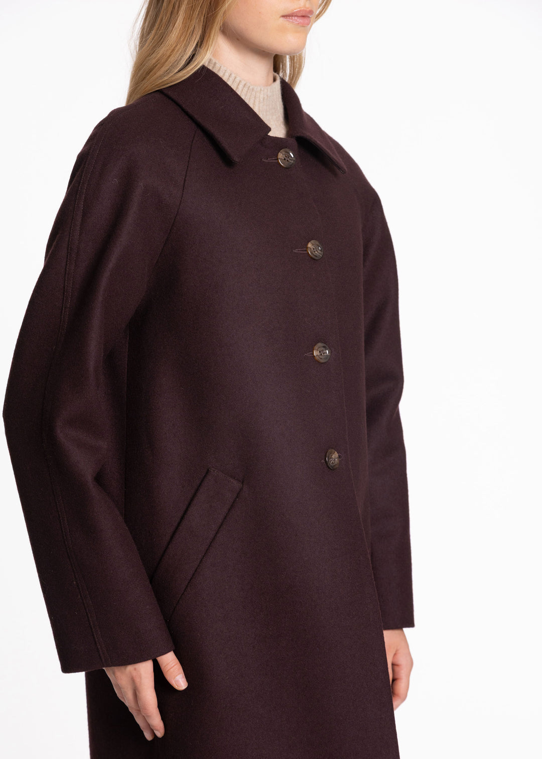 A woman wearing a dark mulberry wool coat with a collar and front buttons, shown from the side against a plain white background.