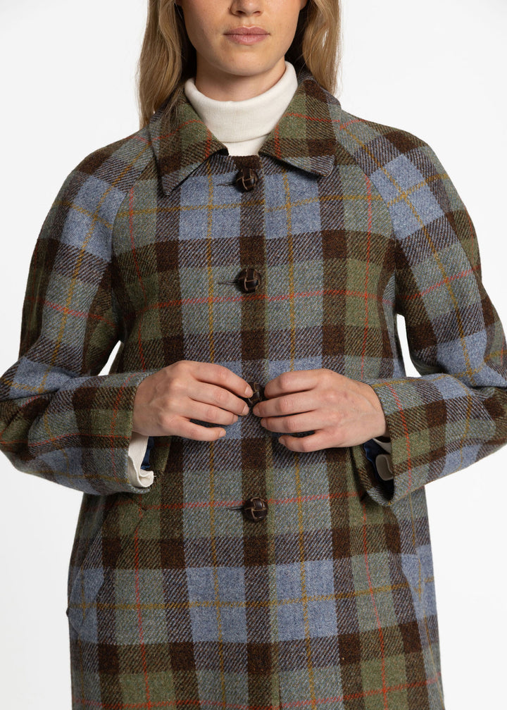 A woman wearing a long plaid coat over a white turtleneck, shown from the mouth down against a plain light background.