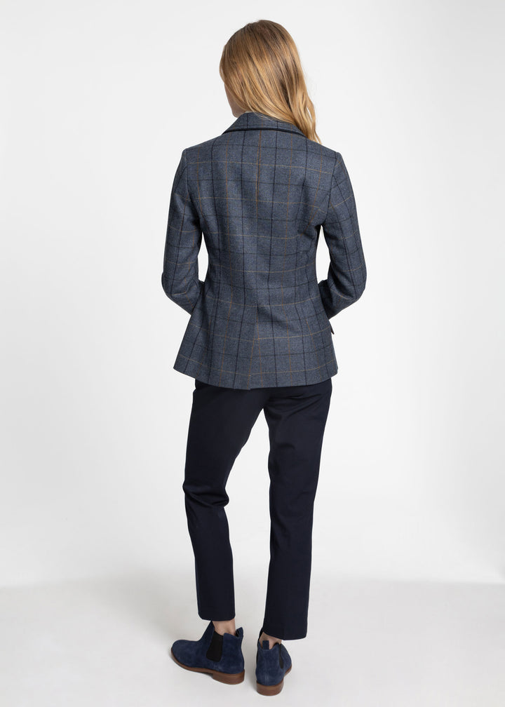 A woman shown from the back wearing a navy blue plaid jacket, dark navy trousers, and navy Chelsea boots against a plain white studio background.