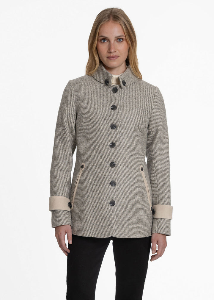 A woman modeling a light beige and gray twill jacket with dark buttons, a high stand collar, and beige cuffs, set against a plain white studio background.