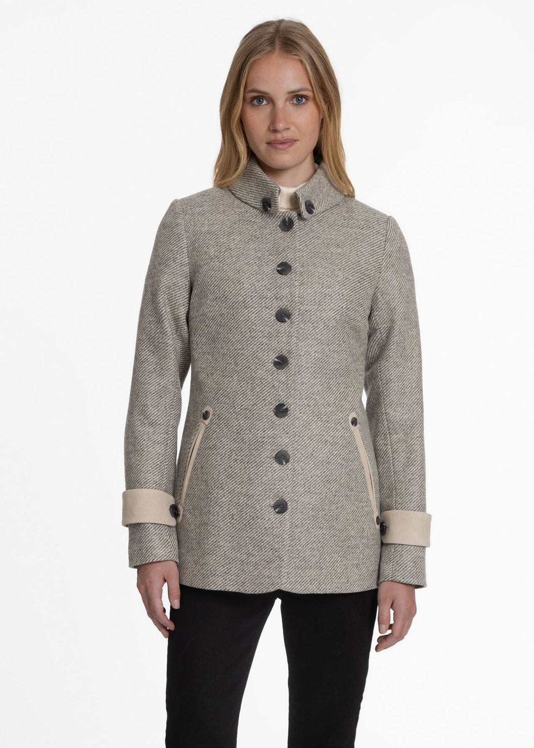 A woman modeling a light beige and gray twill jacket with dark buttons, a high stand collar, and beige cuffs, set against a plain white studio background.