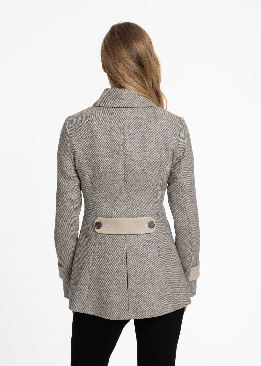 A woman viewed from the back wearing a light gray and beige twill jacket with beige pockets and a beige waist belt, paired with black pants, against a plain white background.