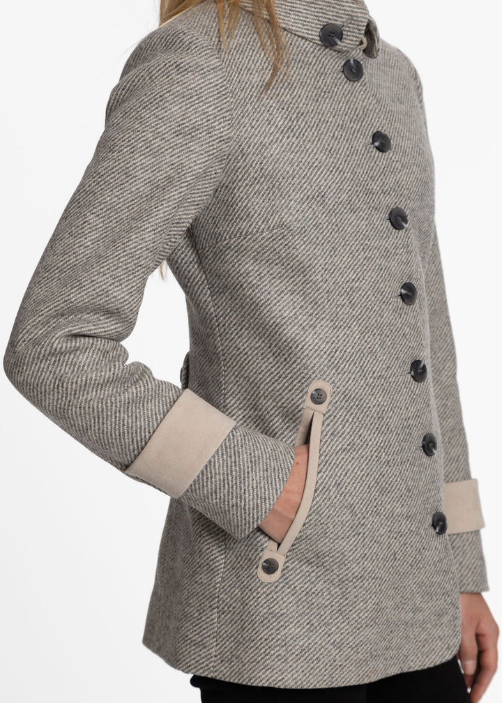 A close-up of a woman wearing a gray and beige twill jacket with dark buttons and beige contrast trim.