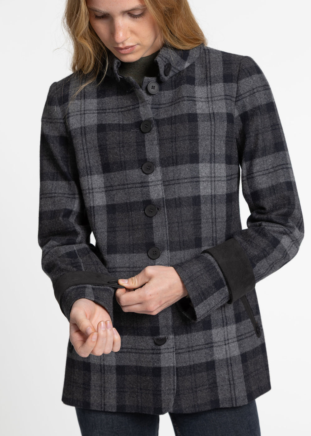 A woman wearing a dark gray and black plaid jacket with black button closures and black cuff bands, shown from the head down against a plain light background.