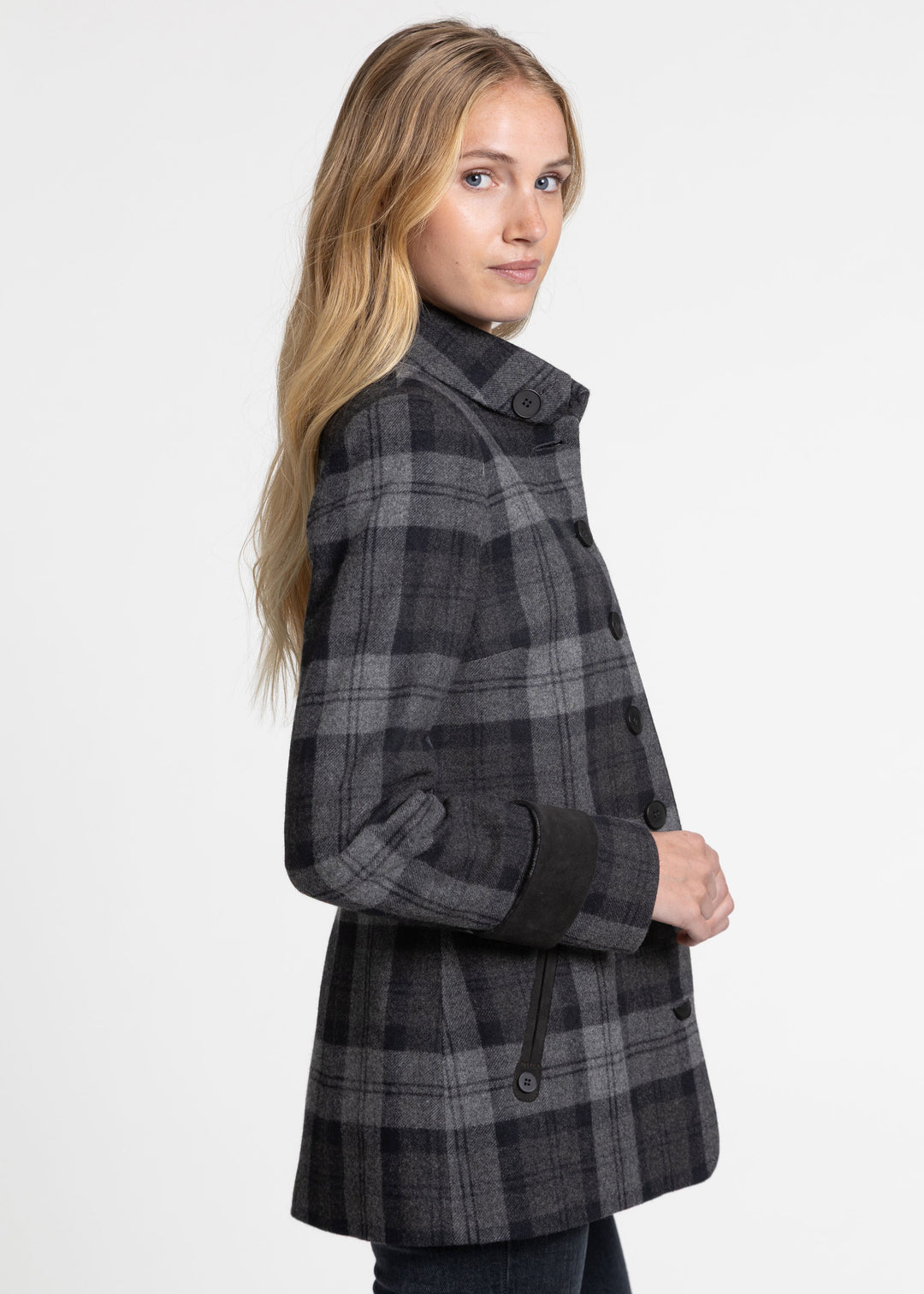 A woman wearing a dark gray and black plaid jacket, shown from a side profile against a plain white studio background.