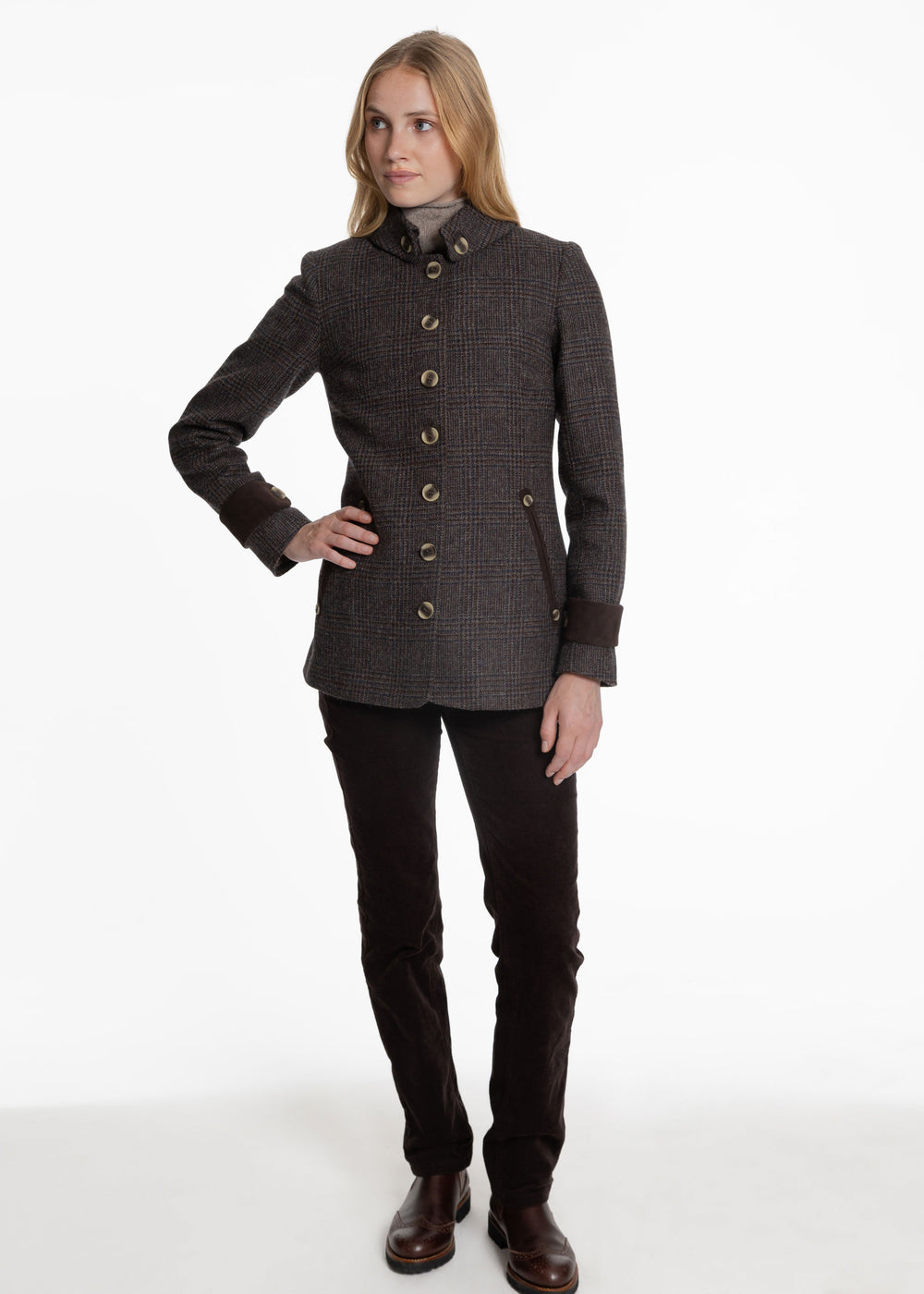 A woman modeling a dark brown and black textured tweed jacket with beige buttons, paired with black pants and brown boots, against a plain white studio background.