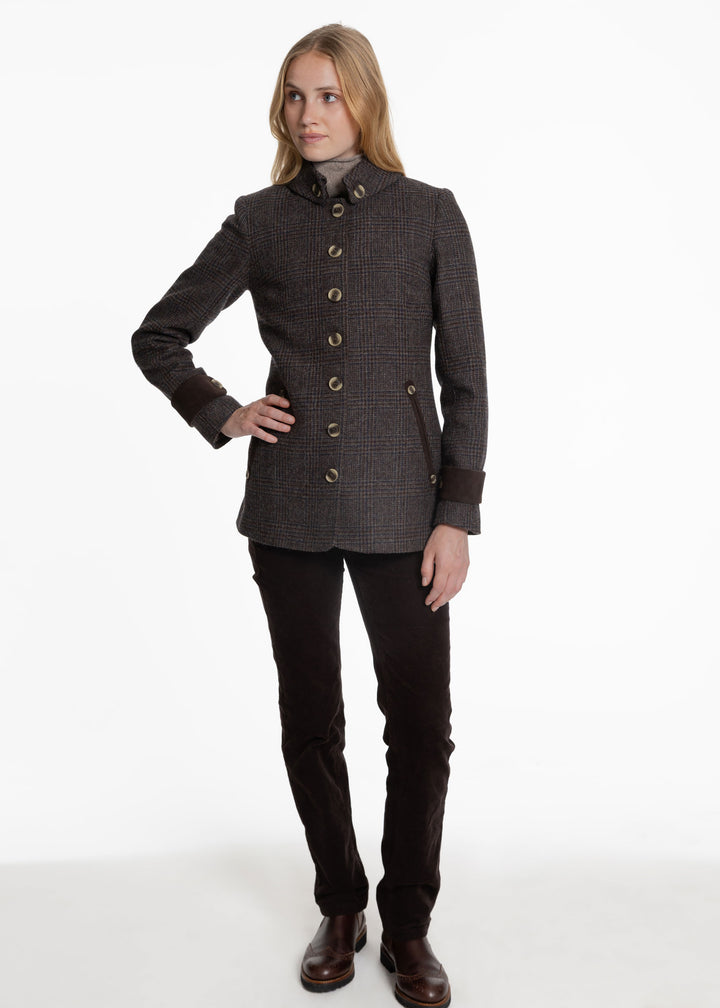 A woman modeling a dark brown and black textured tweed jacket with beige buttons, paired with black pants and brown boots, against a plain white studio background.