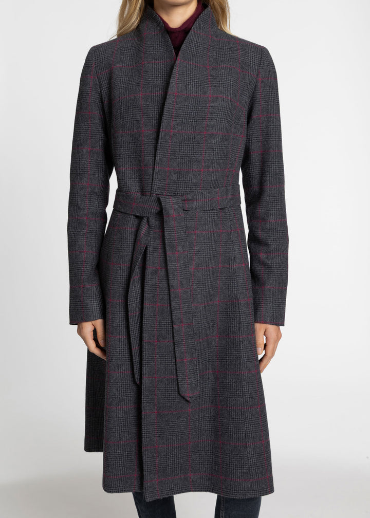 A woman wearing a dark gray belted wrap coat with a subtle red windowpane plaid pattern, shown from the neck down against a plain light gray studio background.