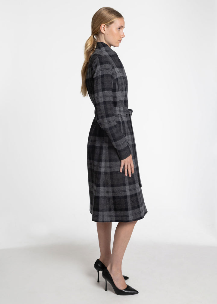 A woman modeling a long-sleeved, knee-length plaid coat in dark gray and black, shown from a side profile against a plain white studio background.