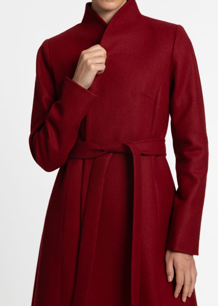 A close-up of a model wearing a long-sleeved, high-neck wrap coat in red, featuring a matching waist tie belt.