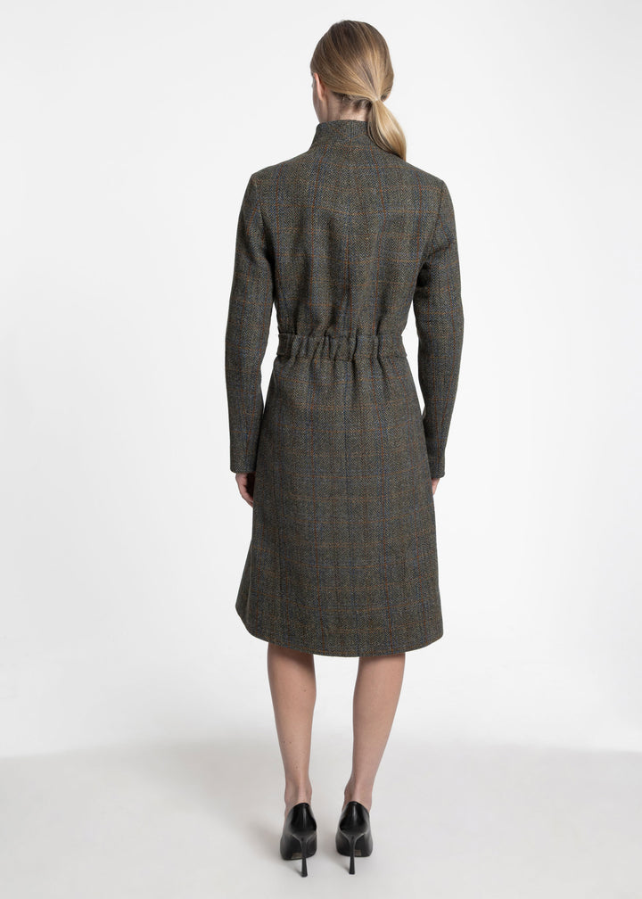 A woman viewed from the back wearing a knee-length plaid coat with a high collar and a self-tie waist belt, paired with black heels, against a plain white studio background.