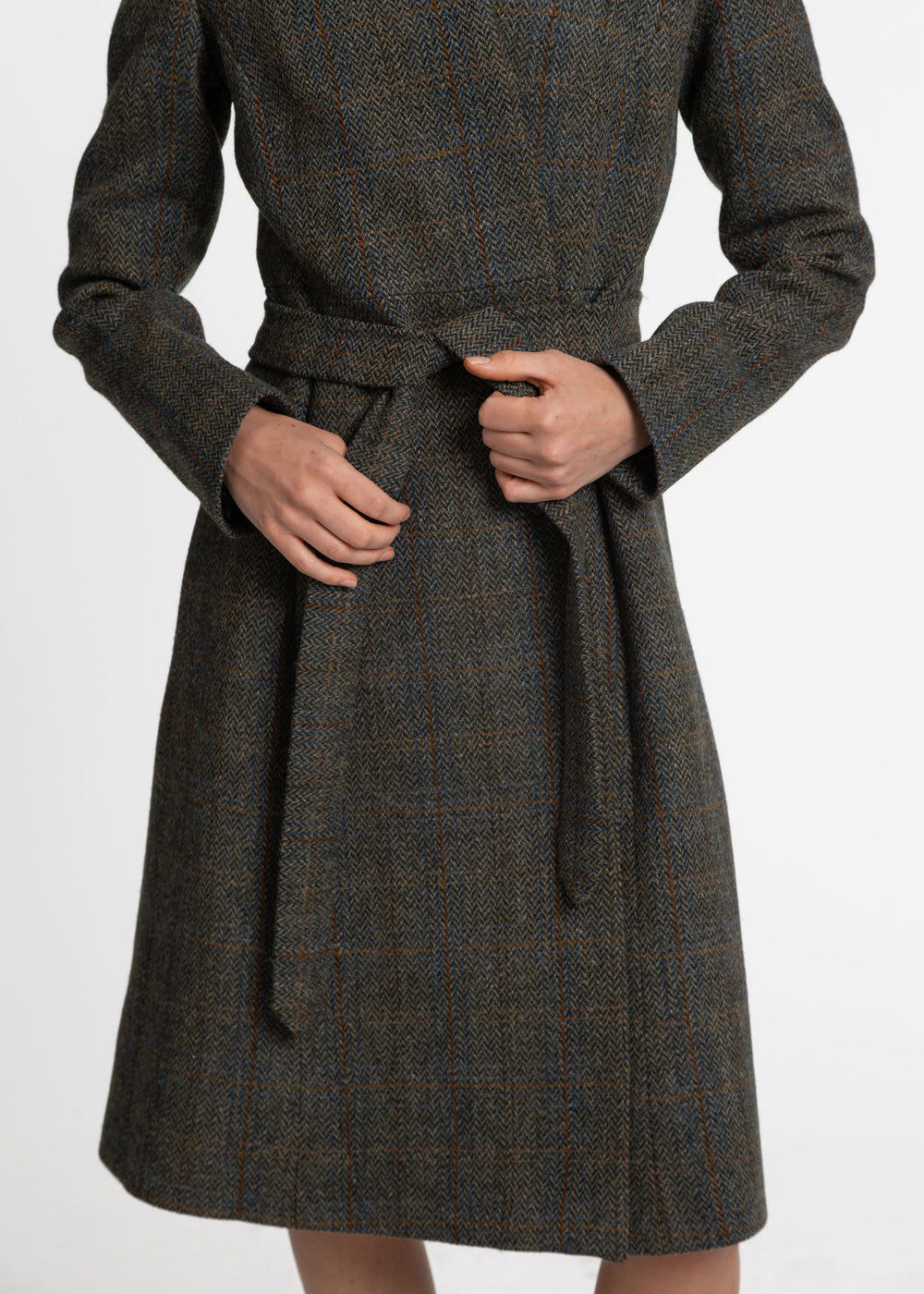 A close-up of a person wearing a dark brown and gray plaid wool coat with a matching waist tie belt, shown from the chest down against a plain white background.