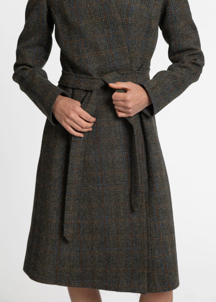 A close-up of a person wearing a dark brown and gray plaid wool coat with a matching waist tie belt, shown from the chest down against a plain white background.