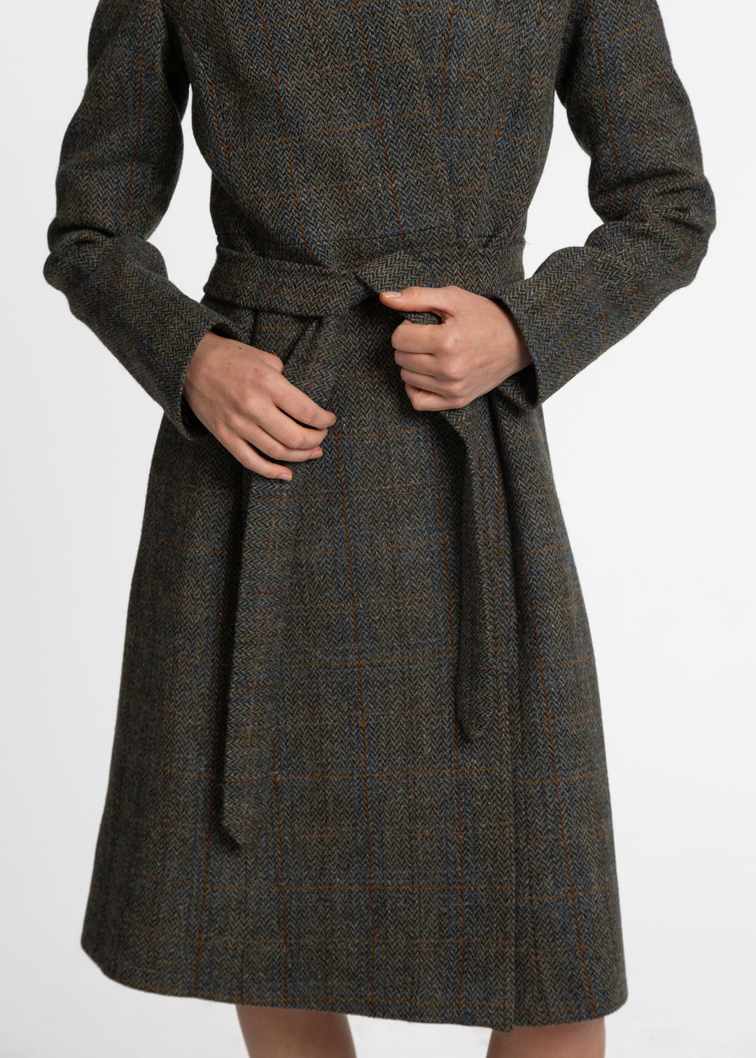 A close-up of a person wearing a dark brown and gray plaid wool coat with a matching waist tie belt, shown from the chest down against a plain white background.