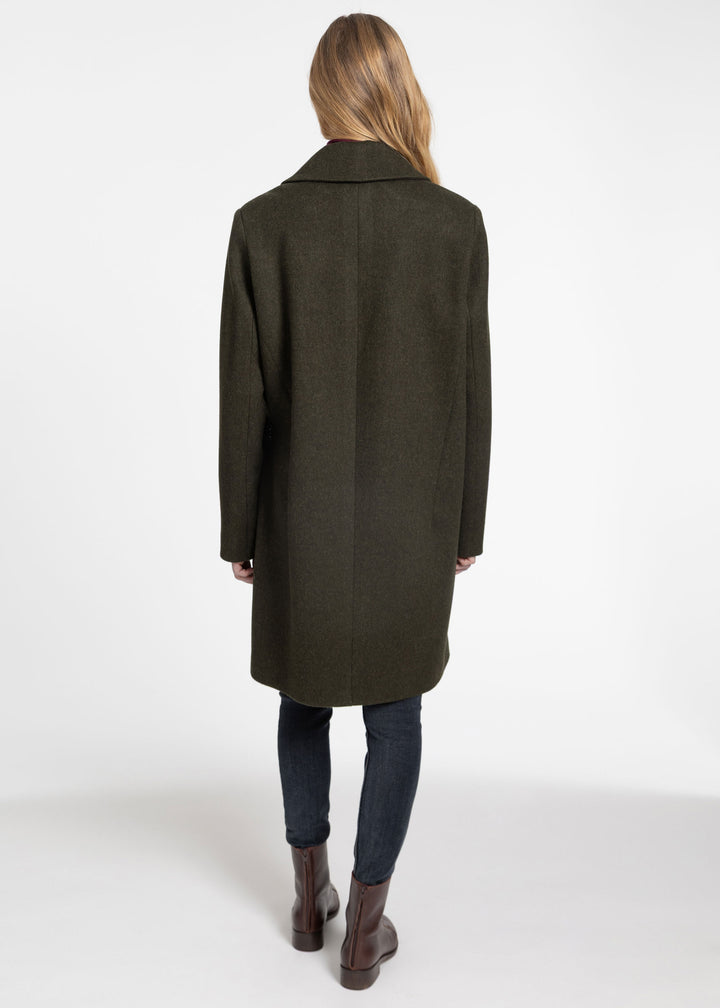 A woman viewed from behind wearing a dark olive green wool coat, dark blue jeans, and brown leather ankle boots against a plain white studio background.