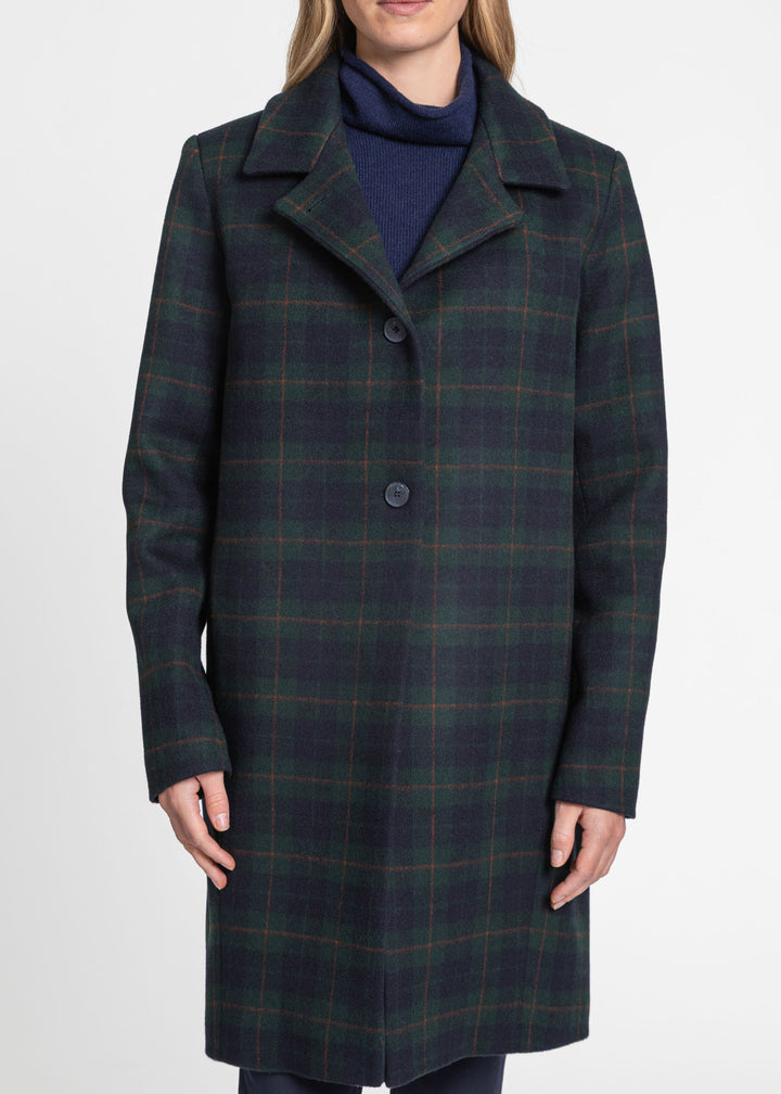 A woman wearing a dark navy and green plaid wool coat over a navy turtleneck sweater, photographed against a clean white studio background.