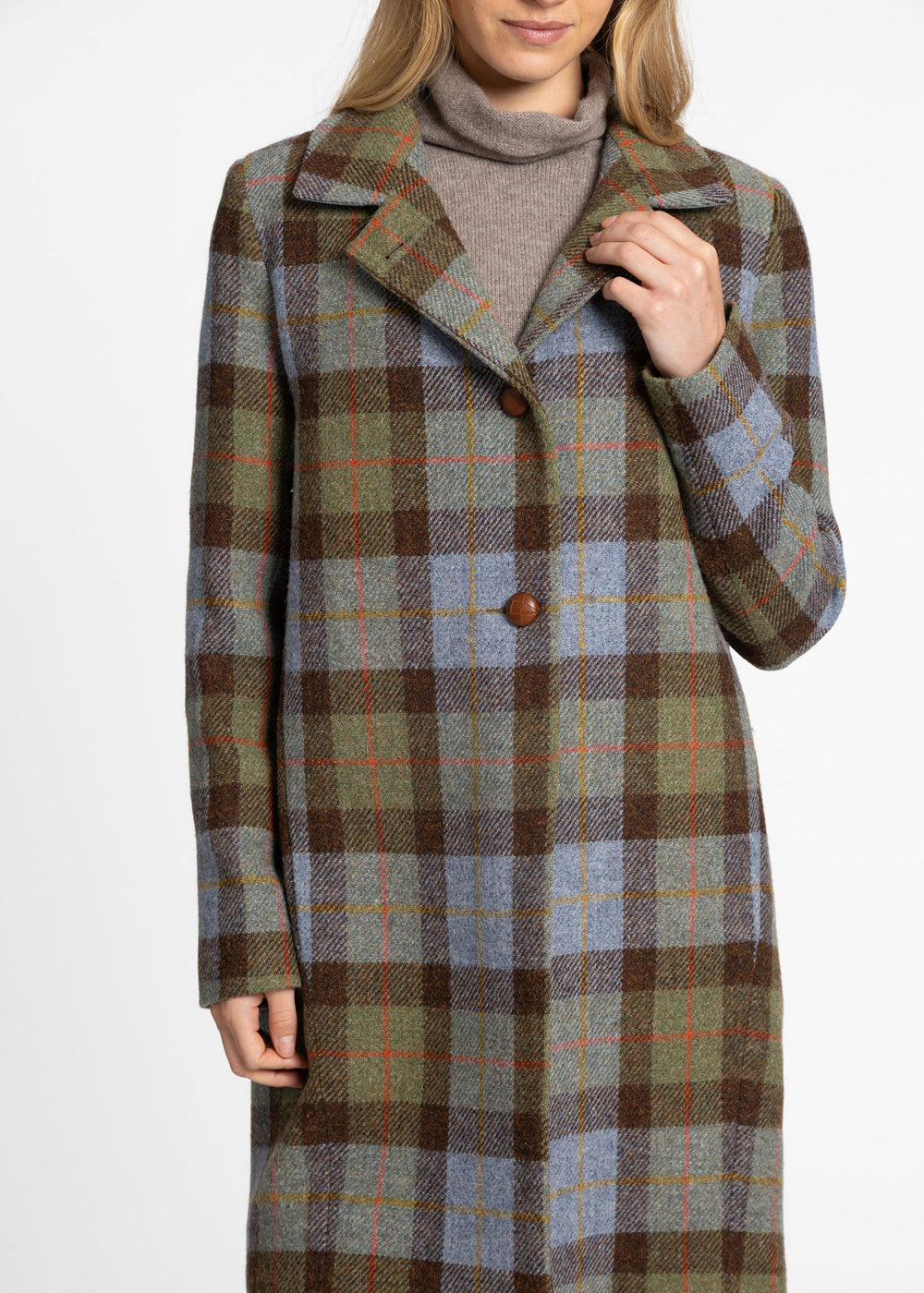 A woman wearing a long plaid coat over a taupe turtleneck sweater, photographed against a plain light gray studio background.