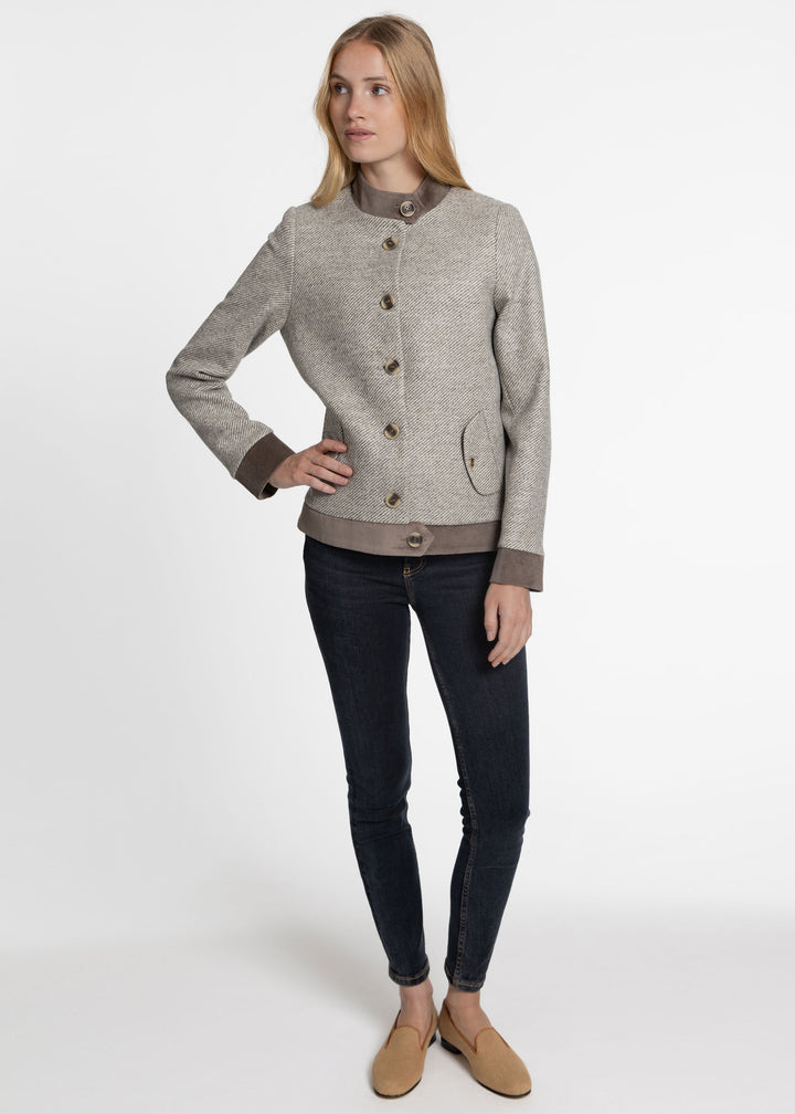 A woman modeling a light gray textured jacket with brown buttons, a brown collar, and brown cuffs, paired with dark skinny jeans and tan loafers, against a plain white studio background.