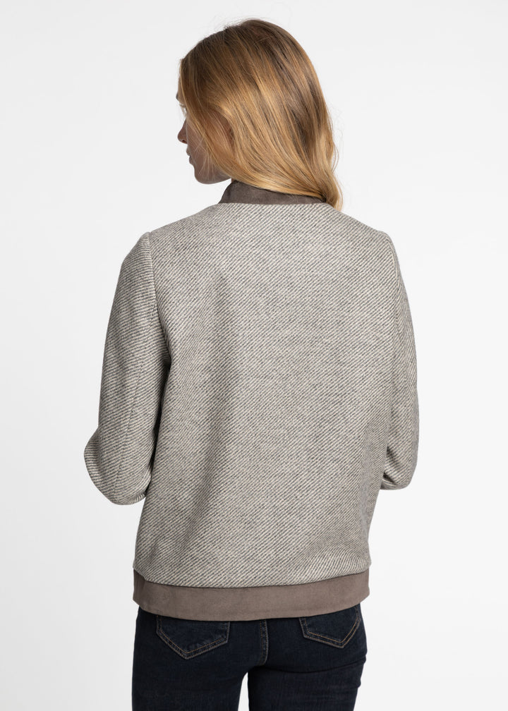 A woman viewed from the back wearing a textured gray jacket with brown trim at the collar, cuffs, and hem, paired with dark blue jeans against a plain white background.