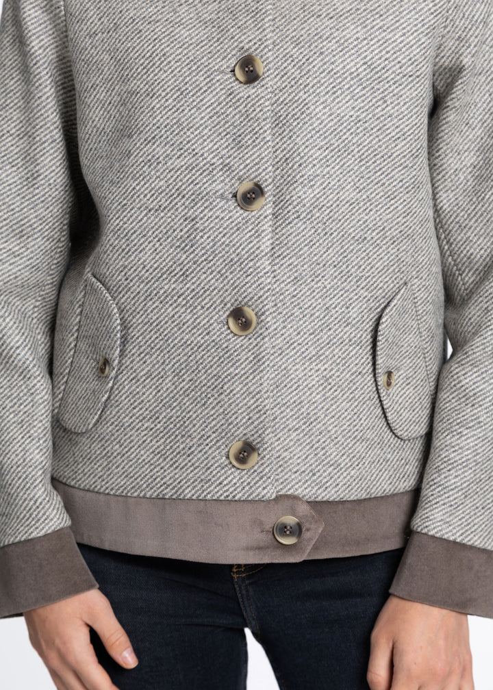 A close-up of a person wearing a gray textured jacket with brown buttons, a brown waistband, and brown cuffs, paired with dark blue jeans.
