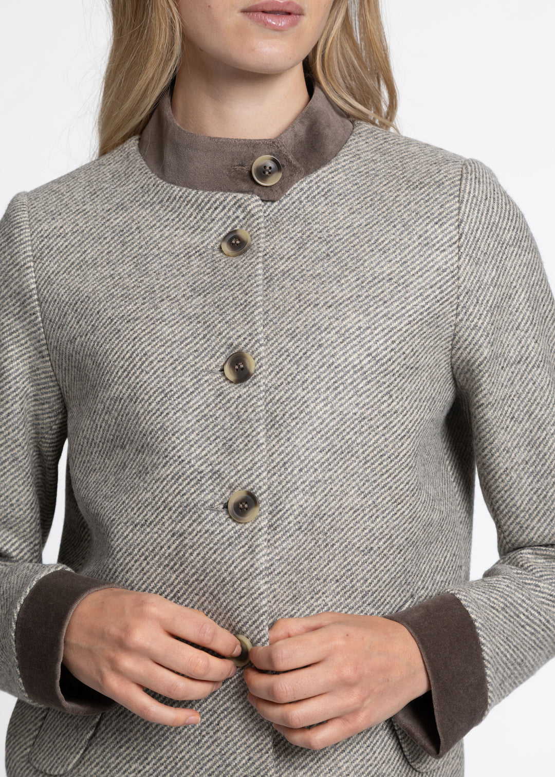 A close-up of a woman wearing a gray and beige jacket with a brown collar and cuffs, buttoned at the front.