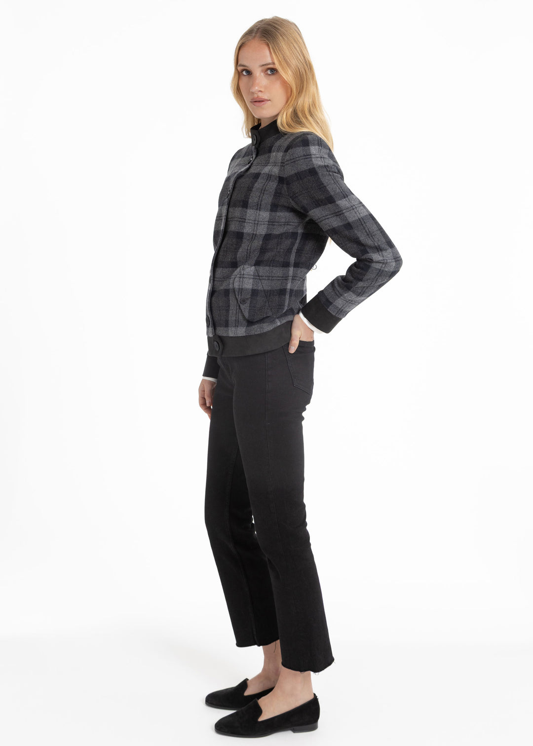 A woman modeling a black and gray plaid jacket and black cropped trousers against a plain white studio background.