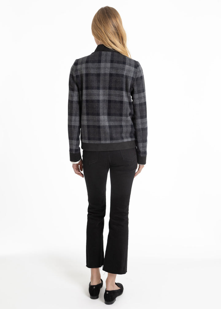 A woman viewed from the back wearing a black and gray plaid jacket, black cropped pants, and black flats against a plain white studio background.
