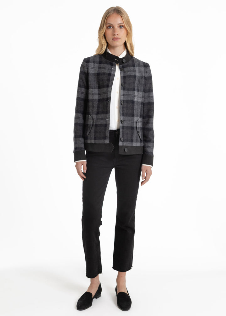 A woman modeling a black and gray plaid cropped jacket with a high collar, worn over a white top and black pants, on a white studio background.