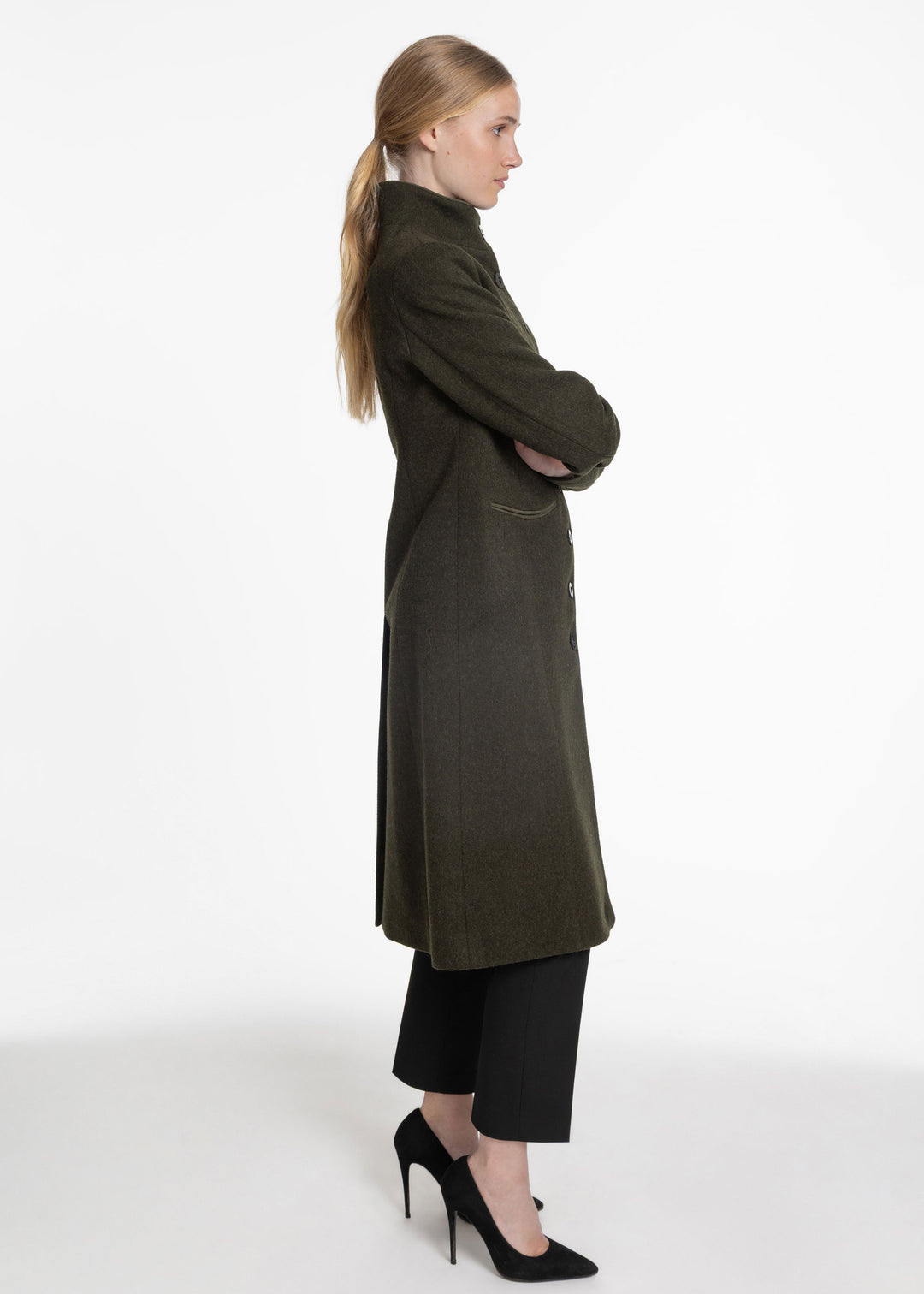 Side view of a woman wearing a dark green wool coat on a white background.