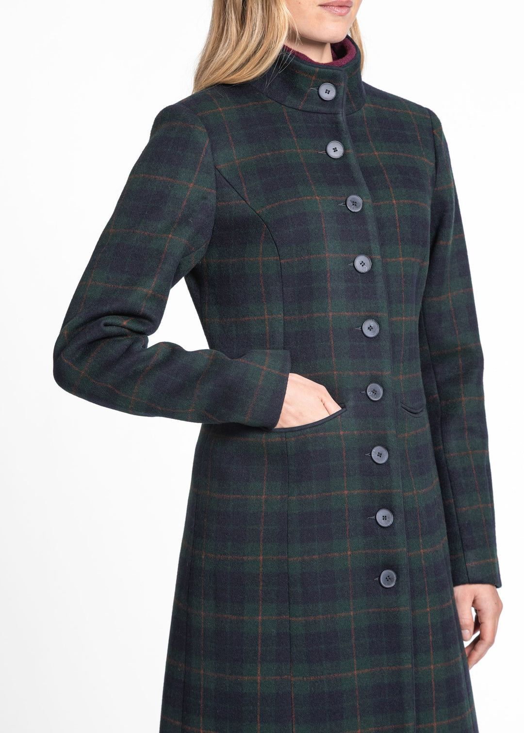 A woman wearing a dark green and black plaid wool coat with red and yellow overcheck lines, featuring a high mock neck and front buttons, shown against a plain white background.