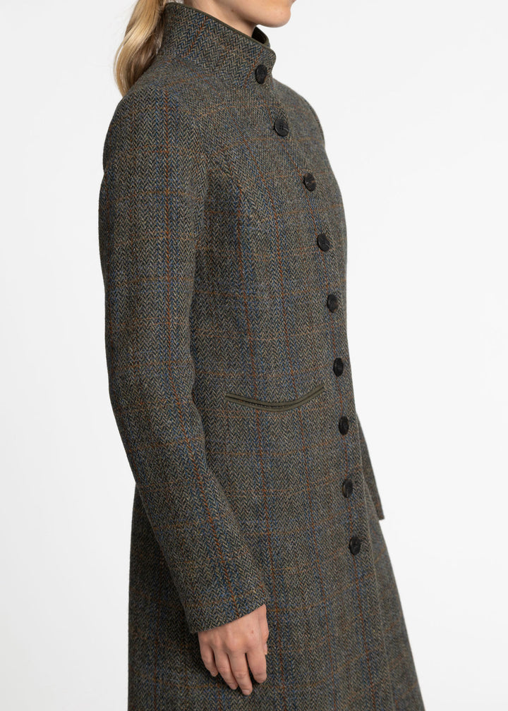 A side profile view of a woman wearing a long, green tweed coat with a high stand collar and dark buttons, set against a plain white background.