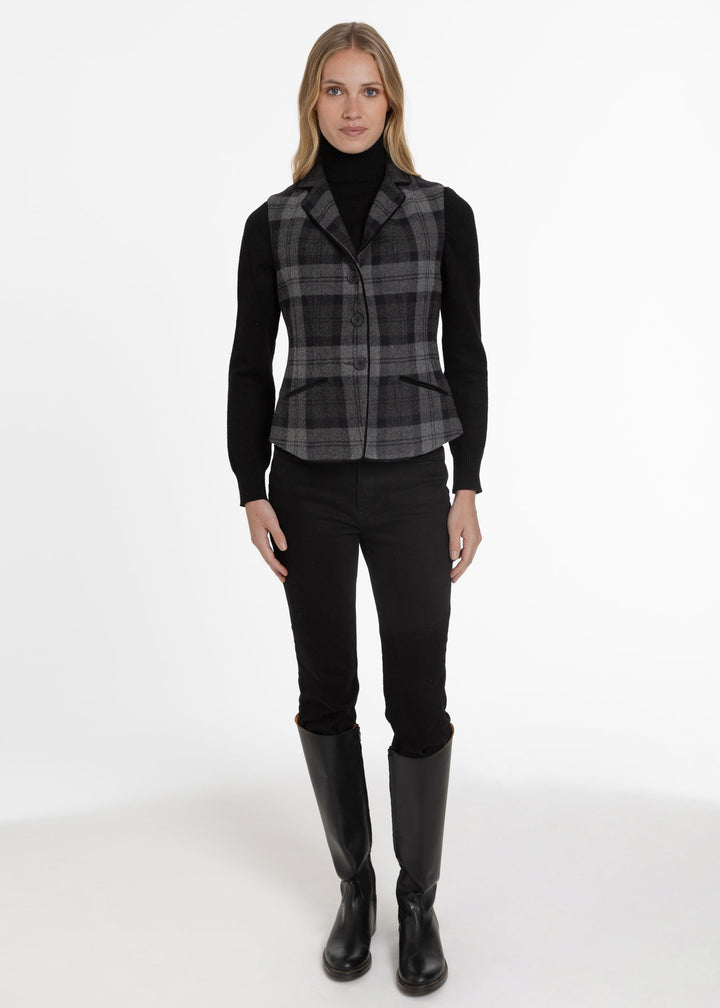 Woman wearing a black and grey plaid waistcoat paired with a black turtleneck sweater, black trousers and boots.