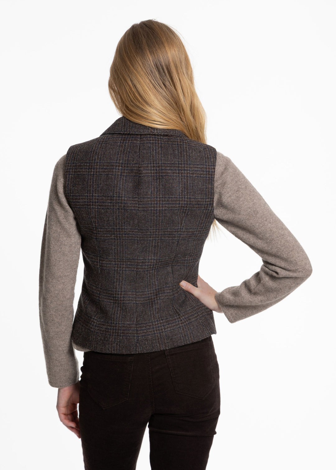 A woman shown from the back wearing a dark black and brown plaid waistcoat over a taupe long-sleeve top and black pants, against a plain white background.