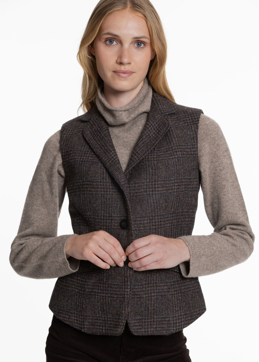 A woman wearing a brown and black check waistcoat over a grey turtleneck sweater.