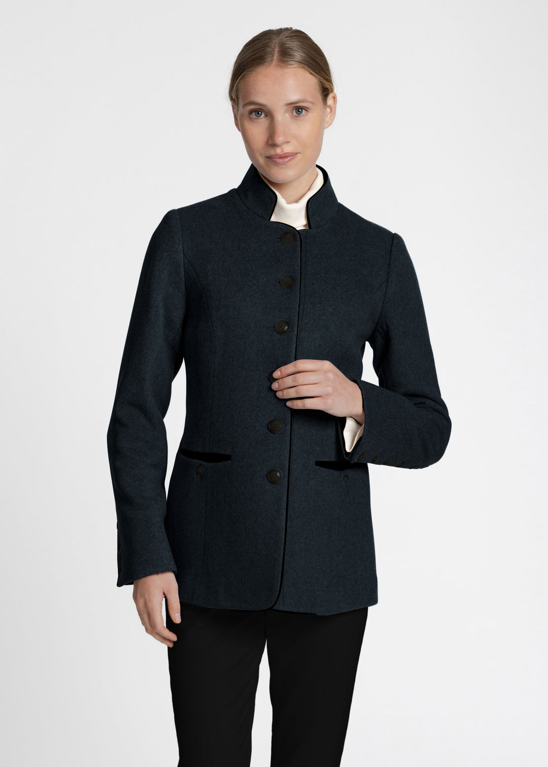 Woman wearing a dark green jacket with a white turtle neck and black jeans.