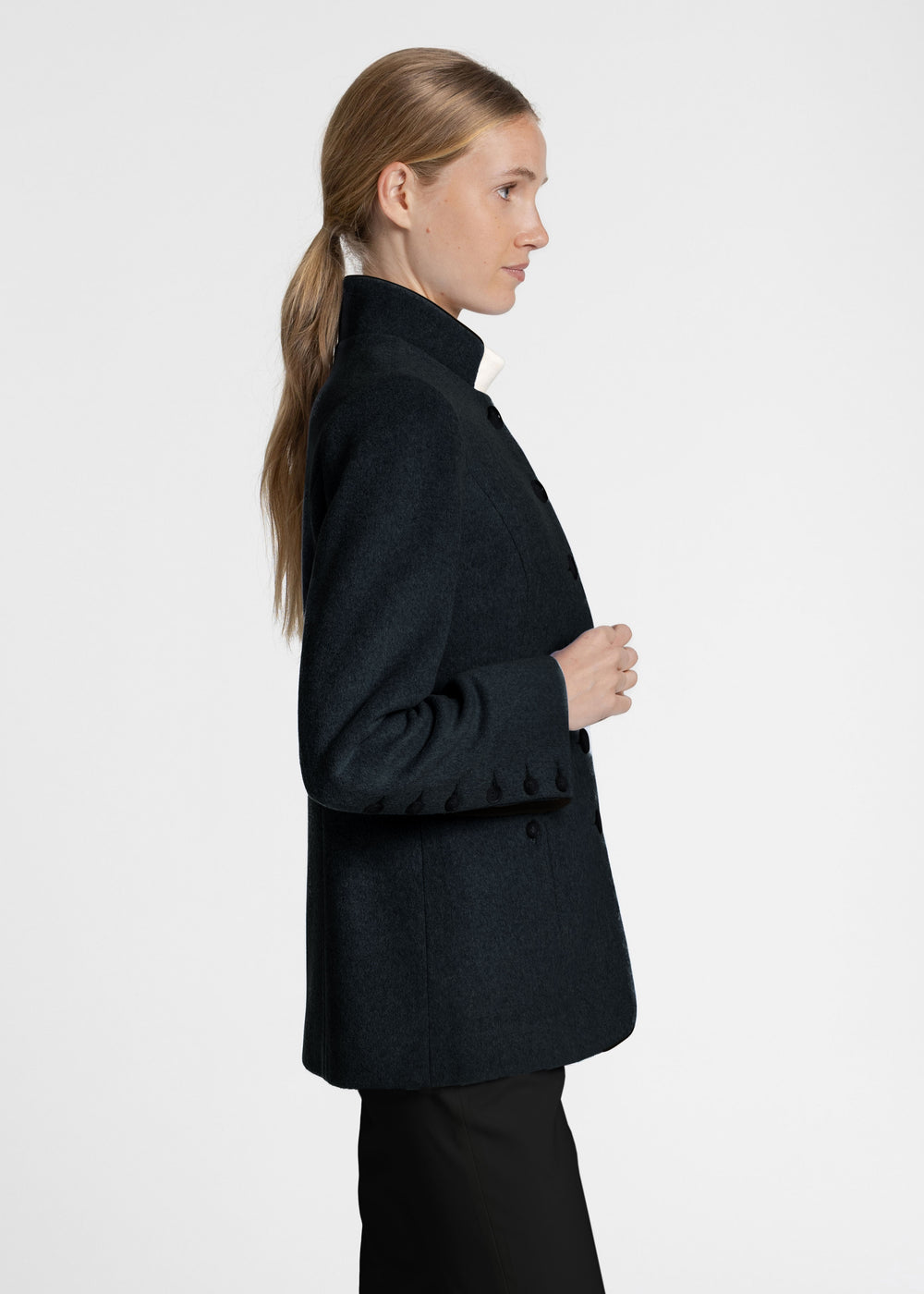 Side view of a woman wearing a dark green jacket with black buttons up the sleeve.