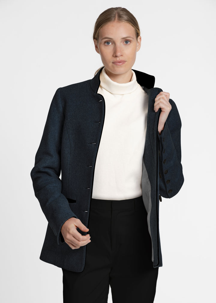 Woman wearing a dark green jacket with a white turtleneck. 