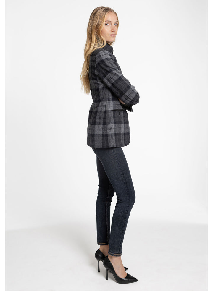 A woman modeling a black and gray plaid jacket, dark skinny jeans, and black high heels against a plain white studio background.