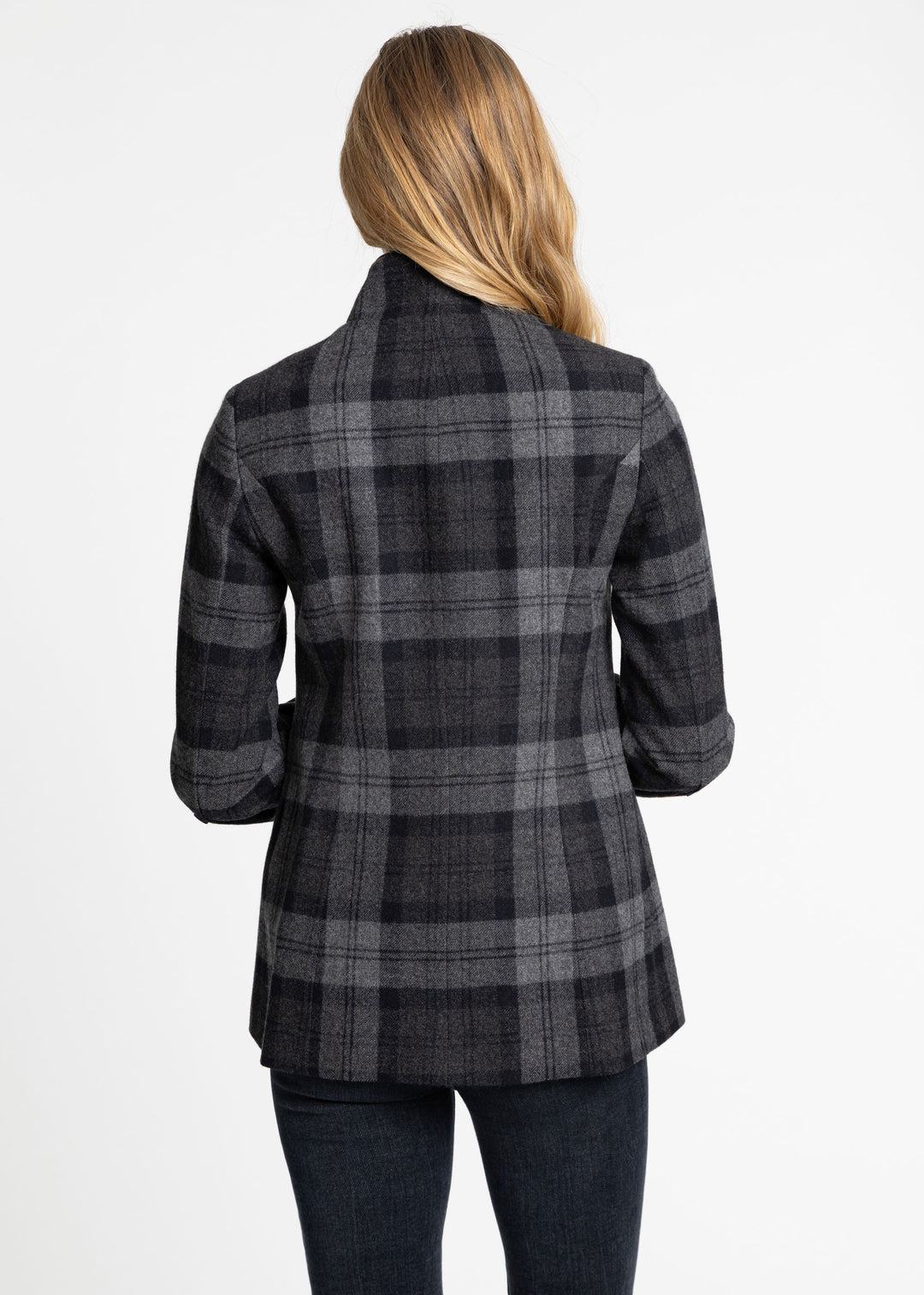 A woman viewed from the back wearing a dark gray and black plaid jacket over a black top and dark jeans, against a plain white studio background.