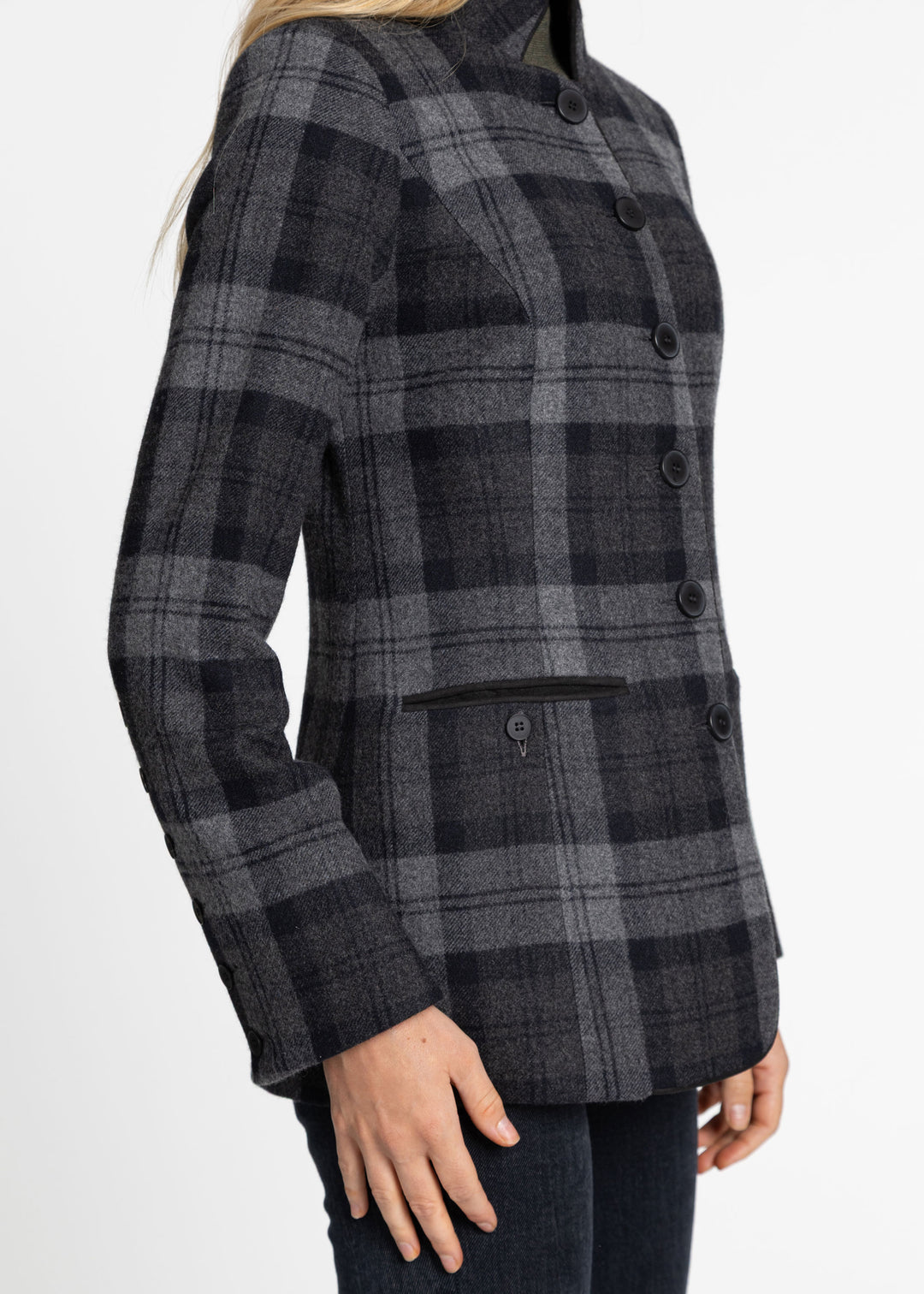 A woman wearing a dark gray and black plaid wool-blend jacket with a high stand collar and front buttons, paired with dark jeans, shown from a side profile against a white studio background.